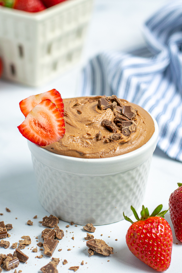 Ramekin filled with silky looking chocolate hummus, topped with beckon off chunks of chocolate and slices of strawberries.
