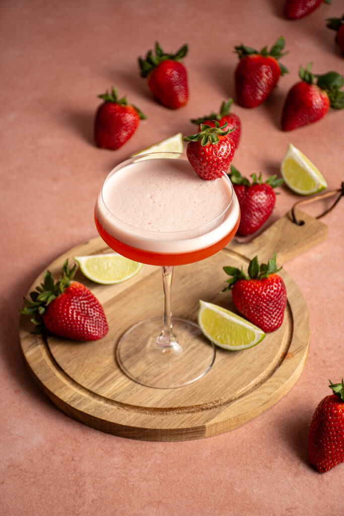 A cocktail glass with a foamy top and strawberry on the edge.